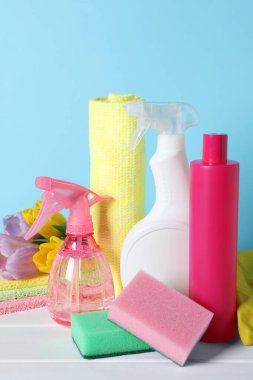 Spring cleaning. Detergents, flowers and sponges on white wooden table against light blue background