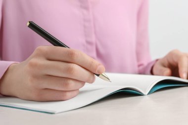 Woman with pen and notepad at white wooden table, closeup