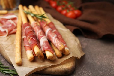 Delicious grissini sticks with prosciutto on brown table, closeup. Space for text