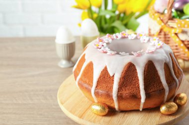Delicious Easter cake decorated with sprinkles near eggs on wooden table, closeup. Space for text