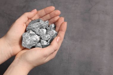 Woman with silver nuggets at grey table, closeup. Space for text