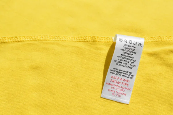Clothing label on yellow garment, top view, Space for text