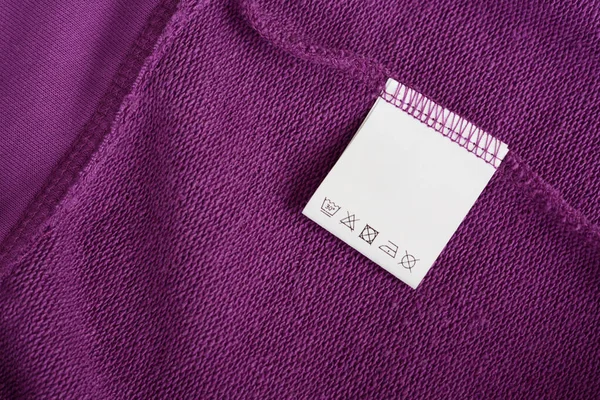 White clothing label with care information on purple garment, top view. Space for text