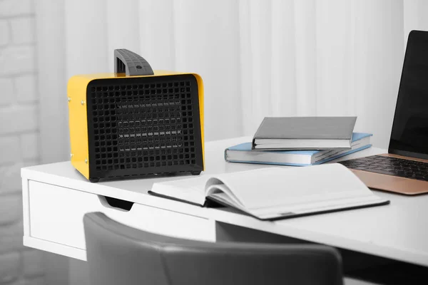 Modern electric fan heater near notebooks on white table in office