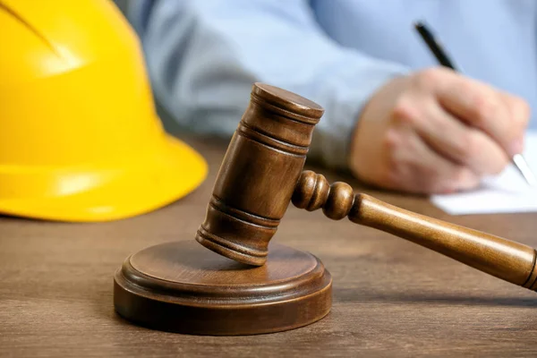 Construction and land law concepts. Man writing at wooden table, focus on gavel