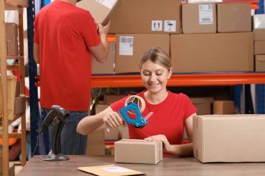 Post office worker packing parcel at counter indoors
