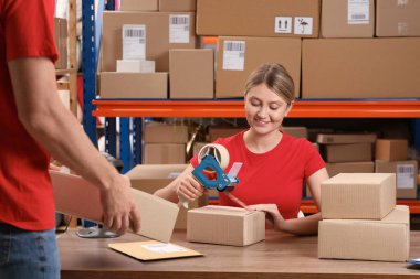 Man with cardboard boxes and woman packing parcel at post office