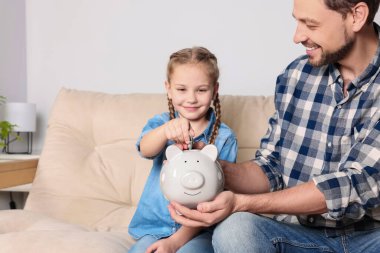 Küçük kız babasıyla birlikte evdeki domuz kumbarasına para yatırıyor.