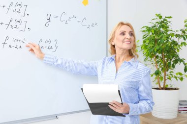 Professor with clipboard giving lecture near whiteboard in classroom