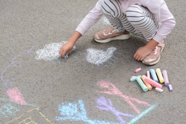 Little child drawing white clouds with chalk on asphalt, closeup