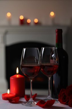 Glasses of red wine, burning candles and rose flowers on grey table indoors. Romantic atmosphere