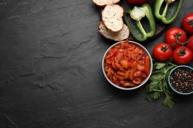 Delicious lecho in bowl and ingredients on black table, flat lay. Space for text
