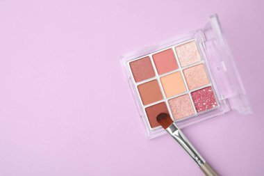 Beautiful eye shadow palette and brush on lilac background, top view. Space for text
