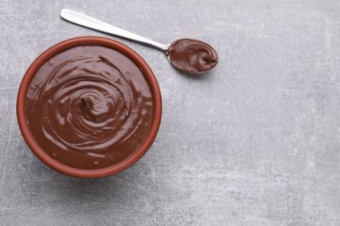 Bowl of chocolate paste and spoon on grey table, flat lay. Space for text