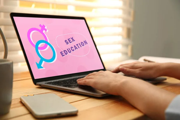 Sex education program. Teenage girl using modern laptop at wooden table, closeup