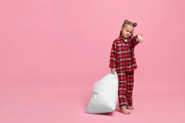 Girl in pajamas with pillow sleepwalking on pink background, space for text