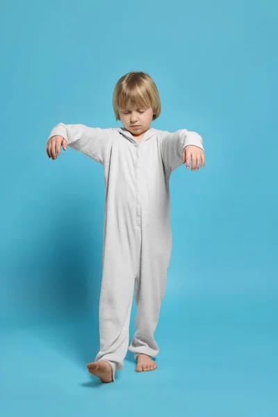 Boy in pajamas sleepwalking on light blue background
