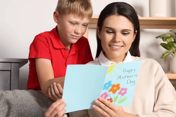 Happy woman receiving greeting card from her son at home