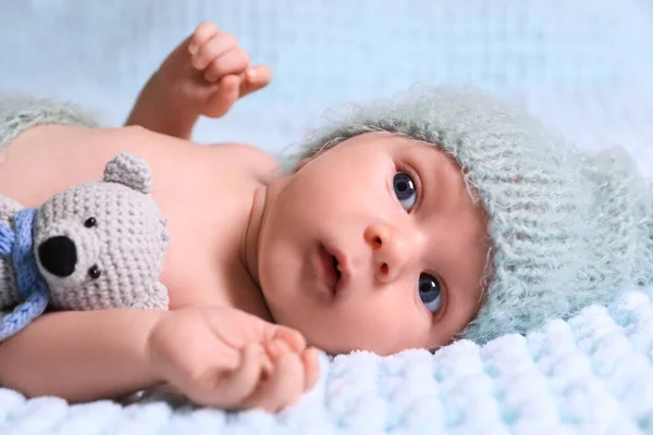 Cute newborn baby with crochet toy on light blue blanket, closeup