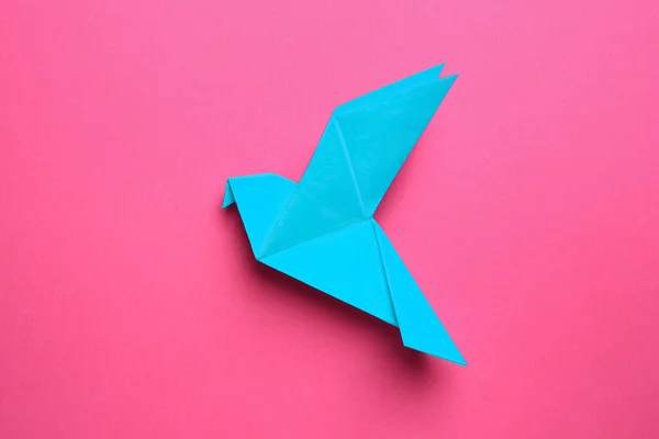 Beautiful light blue origami bird on pink background, top view