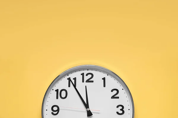 Clock showing five minutes until midnight on yellow background, top view with space for text. New Year countdown