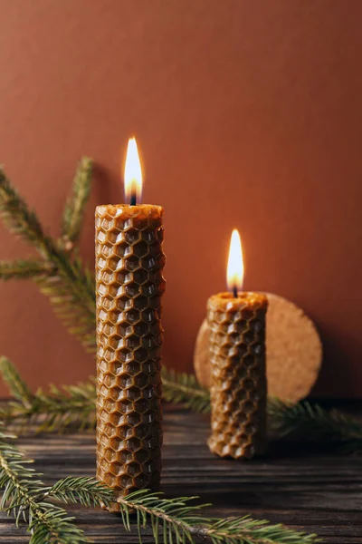 Stylish burning beeswax candles with spruce branches on wooden table
