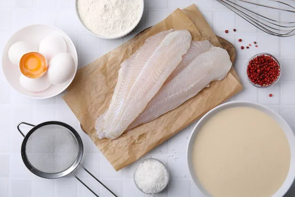 Different ingredients for batter and raw fish fillet on white tiled table, flat lay