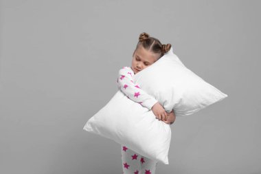 Girl in pajamas hugging pillow on gray background, space for text