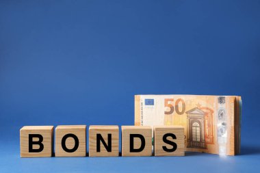 Word Bonds made of wooden cubes with letters and euro banknotes on blue background