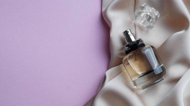 Luxurious bottle of perfume and beige silk on pink background, top view. Space for text