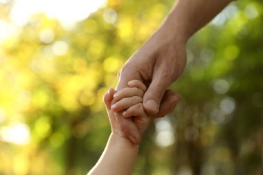 Daughter holding father's hand outdoors, closeup. Happy family