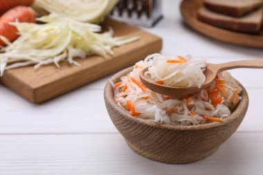 Bowl of tasty sauerkraut on white wooden table, space for text