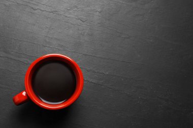 Red cup with aromatic coffee on black textured table, top view. Space for text