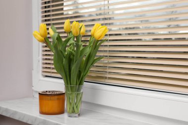 Wonderful tulips and candle on window sill indoors, space for text. Spring atmosphere