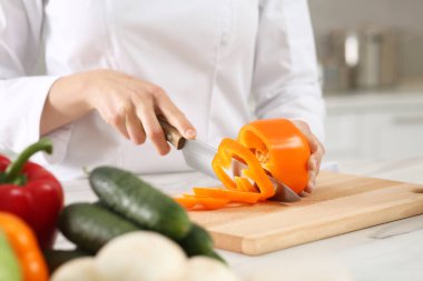 Professional chef cutting cut bell pepper at white marble table in kitchen, closeup