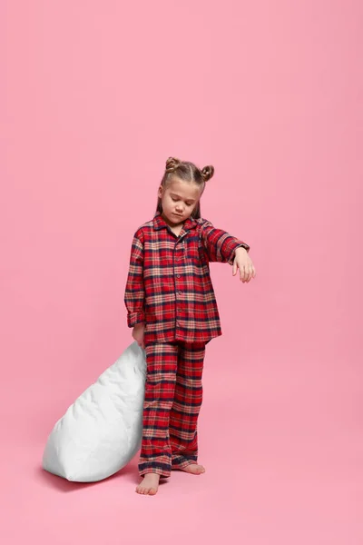 Girl in pajamas with pillow sleepwalking on pink background