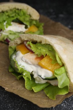 Delicious pita sandwiches with chicken breast and vegetables on parchment paper, closeup