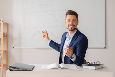 Happy teacher explaining mathematics at table in classroom