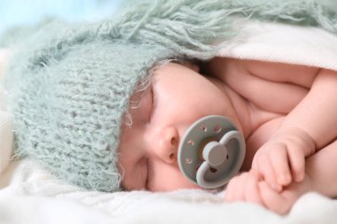 Cute newborn baby with pacifier sleeping on white blanket, closeup