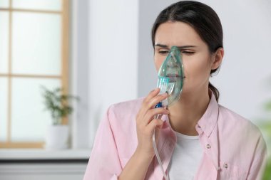 Sick young woman using nebulizer at home, space for text