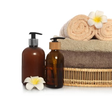 Soft towels in wicker basket, bottles of cosmetic products and plumeria flowers on white background