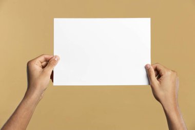 Man holding sheet of paper on beige background, closeup. Mockup for design