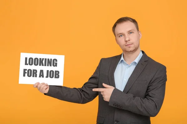 Unemployed man pointing at sign with phrase Looking For A Job on orange background