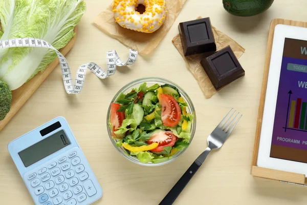 Tablet with weight loss calculator application, tasty salad and other food on wooden table, flat lay