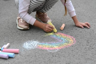 Little child drawing rainbow with chalk on asphalt, closeup