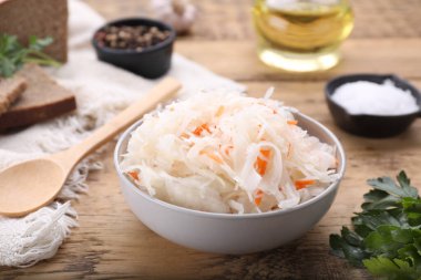 Bowl of tasty sauerkraut and ingredients on wooden table