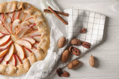 Delicious apple galette, cinnamon and pecans on white wooden table, flat lay