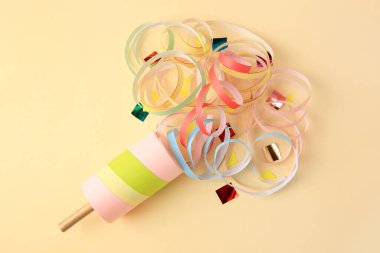 Beautiful serpentine and confetti bursting out of party popper on beige background, flat lay