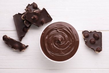 Bowl with tasty paste and pieces of chocolate on white wooden table, flat lay. Space for text