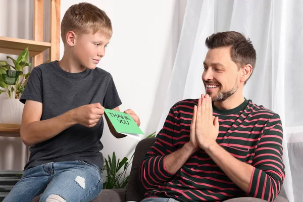 Happy man receiving greeting card from his son at home